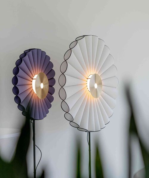 Zwei runde Wandlampen mit gefalteten Schirmen in Weiß und Violett leuchten an einer hellen Wand.
