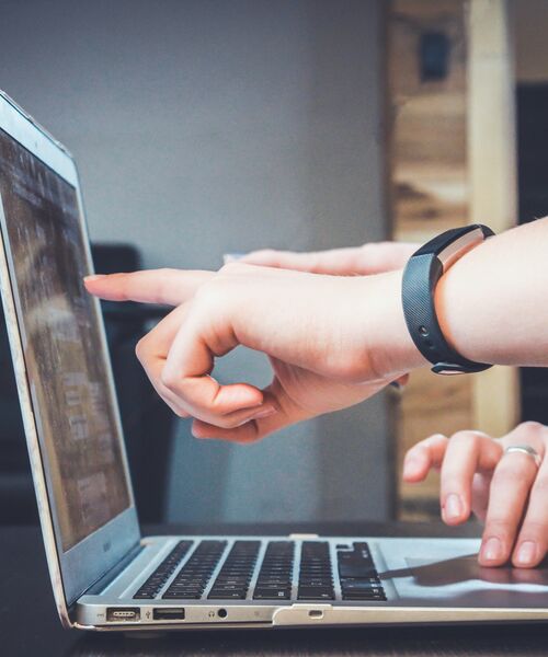 Zwei Hände arbeiten gemeinsam an einem Laptop, eine Person zeigt auf den Bildschirm.