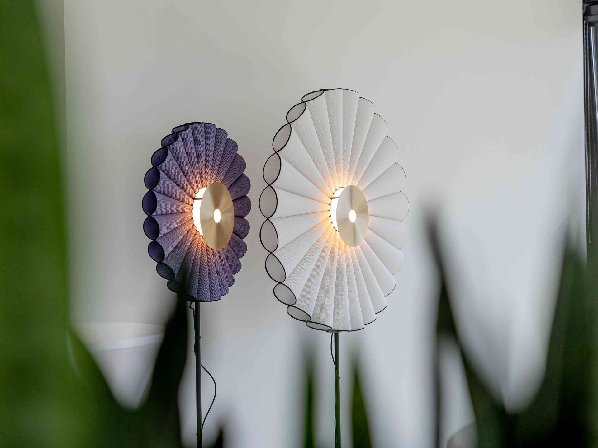 Zwei runde Wandlampen mit gefalteten Schirmen in Weiß und Violett leuchten an einer hellen Wand.