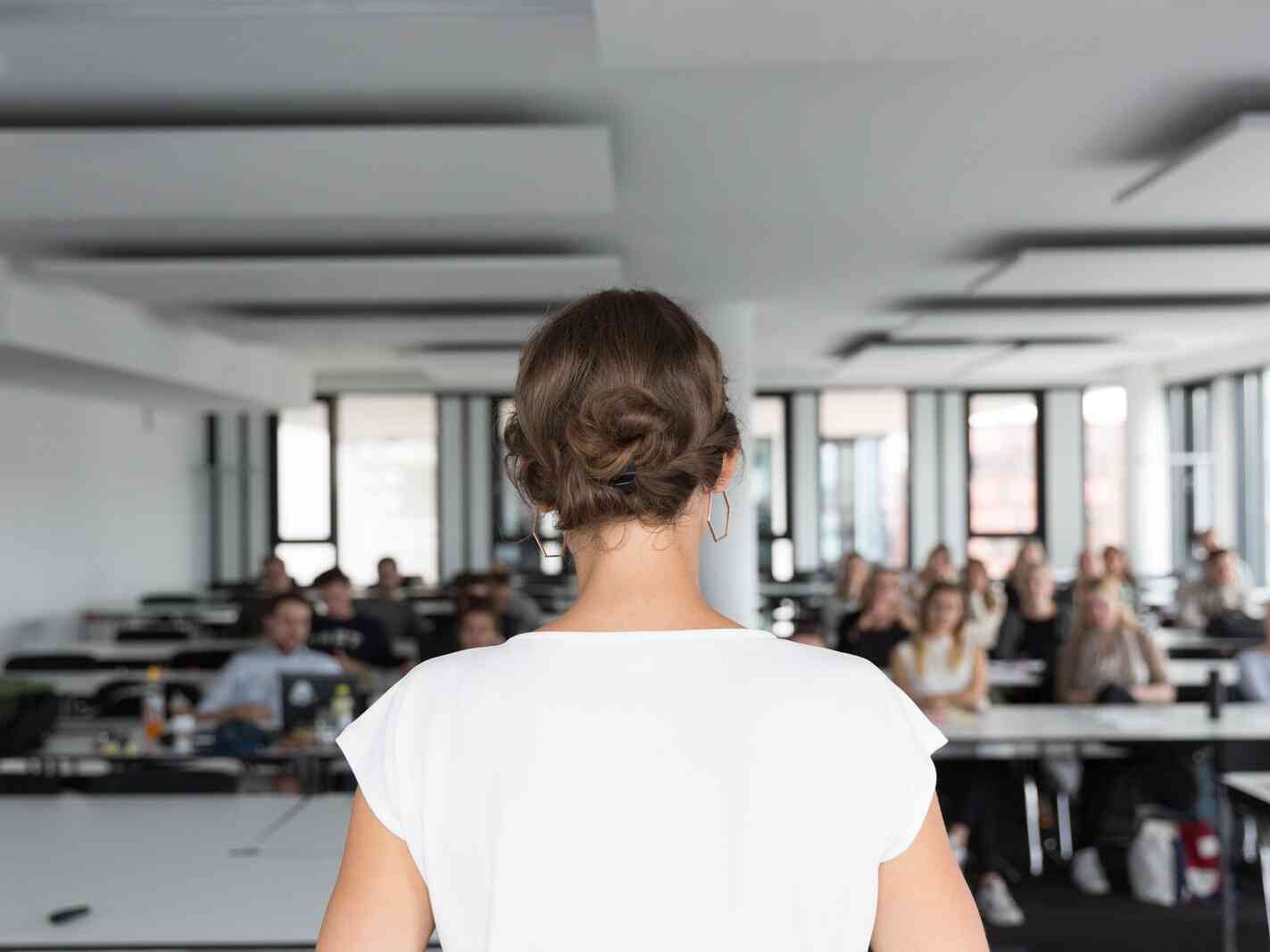 Frau steht vorne im Raum und spricht vor einer Gruppe von Zuhörerinnen und Zuhörern.