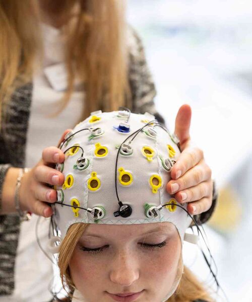 Person trägt eine EEG-Messkappe mit Elektroden, während eine zweite Person die Kontakte überprüft.